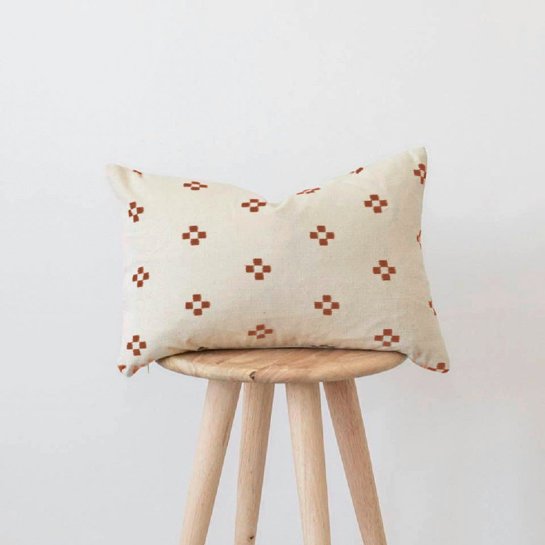 IKAT rusted lumbar cushion, cream with rust ikat crosses, on a wooden stool